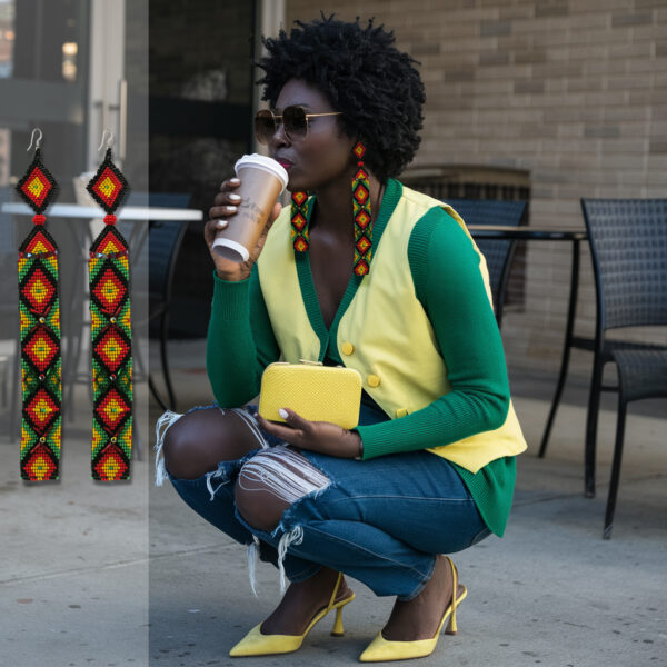 Woman wearing handcrafted Rasta beaded statement earrings in red, gold, green, and black with matching artisan earrings displayed beside her. Bold reggae-inspired statement earrings with colorful beadwork and lifestyle styling.